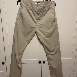 Beige chinos från Filippa K - Snygga beige chinos/kostymbyxor från Filippa K i klassisk rak modell. Byxorna är knappt använda, i nyskick.