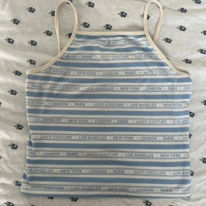 Randig linnetopp Juicy Couture M - Supersöt vintage randig linnetopp från Juicy Couture Black Label i ljusblått och vitt. Tunt material i bomull med lite stretch, smala axelband och tryck med städer och logga över hela toppen. Perfekt för en chill sommardag eller när du vill ha en retro vibe.