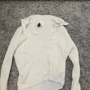 Ribbad vit omlott-tröja Divided XS - Snygg ribbad omlott-tröja från Divided i en ljusvit nyans. Tröjan har v-ringning, lång ärm och är tillverkad i mjuk stickad bomullsmix. Perfekt för lager-på-lager och passar till både jeans och kjol.