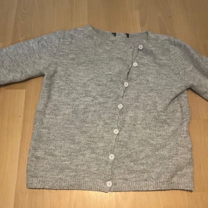 Ljusgrå stickad kofta med knappar - Mysig ljusgrå stickad kofta med rund hals och vita knappar hela vägen framtill. Koftan har lång ärm och ribbade muddar vid ärmslut och nederkant. Perfekt för lager-på-lager och enkel att matcha med olika outfits💕💕 tröjan passar på en Xs, S och även M.