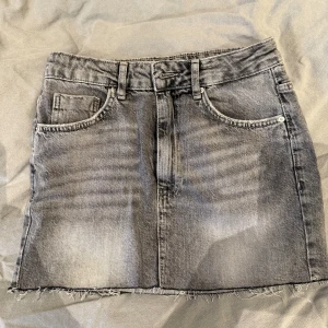 Grå jeanskjol från Pull&Bear - Grå jeanskjol från Pull&Bear i storlek S. Kjolen är kort med fransig kant nertill samt dragkedja och knapp framtill. Säljes pga att den endast ligger i garderoben och är även använd ett väldigt fåtal gånger 😊