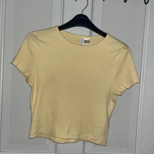 Gul topp från H&M Divided - Söt ljusgul topp från H&M Divided. Modellen är ribbad med rund halsringning och korta ärmar. Perfekt för dig som gillar en enkel och fräsch stil. Toppen är i mjuk bomull och passar perfekt till jeans eller kjol.