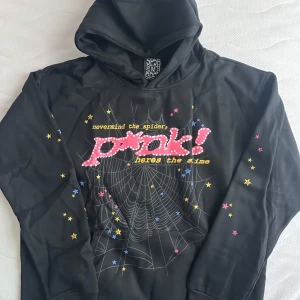Svart hoodie SP5R med stjärnor och tryck - Svart hoodie från SP5R i storlek M med färgglada stjärnor på ärmarna och coolt tryck framtill med texten 'pink! nevermind the spider, here’s the slime' och spindelnätsmotiv. Mjuk insida och huva, perfekt för dig som gillar streetstyle.