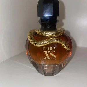 Pure XS parfym från Paco Rabanne - Cool parfymflaska från Paco Rabanne, Pure XS, med en lyxig guldig orm som slingrar sig runt halsen. Flaskan är bärnstensfärgad och har en svart, facetterad kork. Perfekt för dig som gillar unika och snygga detaljer på parfymhyllan.