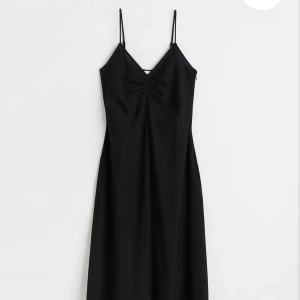 Svart långklänning med smala axelband - Säljer en elegant svart långklänning med smala axelband och v-ringning. Klänningen har en slits framtill och en figurnära passform som ger en stilren siluett. Perfekt för speciella tillfällen när du vill känna dig extra snygg.