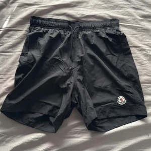 Moncler Badshorts - Snygga svarta Moncler shorts oanvända. Bada i stil o klass, funkar såklart och använda vid vardagliga tillfällen också. Pris kan diskuteras vid snabb affär.