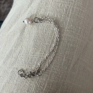 Silverarmband med pärldetalj - Stilrent armband i silverfärgad metall med dubbla kedjor och en vit pärla som detalj. Perfekt för dig som gillar minimalistiska smycken med en liten twist. Lätt att matcha med andra accessoarer. Aldrig använd 