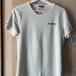 Reebok t-shirt - Riktigt skön modell med stretch; 92% bomull och 8% elastan. Perfekt skick, vit med nyansen ”gammaldags vanilj”. Det är juniorstorlek men den funkar utmärkt för vuxen. Måtten är 86 cm bröstvidd och 61 cm längd vilket motsvarar vuxenstorlek S. Jag har L och har inga problem att få på mig denna, men självklart blir den då spännig. Så skulle säga att den även kan passera som M, med tanke på stretchen. Är du rippad är denna t-shirt en dröm. Upphämtning i Stockholm fungerar.