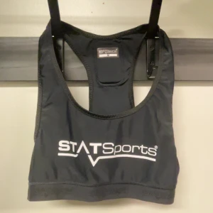 Svart sporttopp från STATSports - Sportig svart linnetopp från STATSports med vitt tryck framtill och bak. Modellen är ärmlös med brottarrygg och elastisk nederkant för extra stöd. Perfekt för träning och aktiviteter där du vill ha maximal rörelsefrihet.