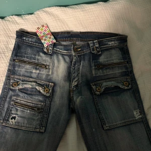 Low waist jeans med unika detaljer - Vintage Low waist jeans med flera fickor med dragkedjor och knappar både fram och bak. Står inte storlek men skulle säga strlk M.
