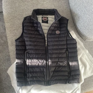 Svart dunväst från Colmar - Snygg svart dunväst från Colmar med quiltad design och dragkedja framtill. Västen har två fickor med dragkedja och hög krage. Perfekt för lager-på-lager och har en stilren look med Colmar-logga på bröstet.