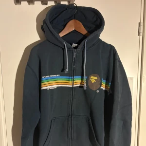 A Bathing Ape (BAPE) hoodie  - Mörkblå hoodie från A Bathing Ape, Bape med dragkedja, huva och snörning.	Står storlek L men passar som en M. Väldigt skön och gosig. Streetwear hoodie	A Bathing Ape stil Grafisk hoodie Oversized hoodie	Vintage streetwear Svart/blå hoodie Second hand hoodie #hoodie #ziphoodie #streetwear #bape #abathingape #vintagehoodie #streetfashion #secondhand #preloved #unisexfashion Osäker om äkta eller fejk