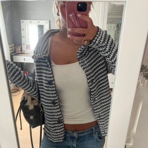 Randig svartvit kofta med stora knappar - Säljer en mysig kofta med svartvita ränder och grov stickning. Koftan har stora svarta knappar hela vägen upp och en bred krage som kan stängas högt. Långärmad och perfekt att slänga över en enkel topp. Passar dig som gillar chill och stilren look. En knapp som sitter lite dåligt men går att fixa(se bild 5)