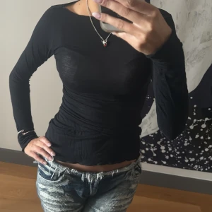 Svart långärmad topp i bomull - Säljer en svart långärmad topp med tight passform och rund hals. Tunt och stretchigt bomullsmaterial som sitter snyggt mot kroppen. Perfekt att styla med jeans eller kjol för en clean look.