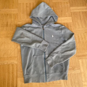 Ralph lauren zip hoodie - Snygg hoodie från Polo Ralph Lauren med dragkedja och klassisk vit broderad logga på bröstet. Tröjan har huva, långa ärmar och två fickor framtill. Tillverkad i mjuk bomull som är skön att ha på sig hela dagen.