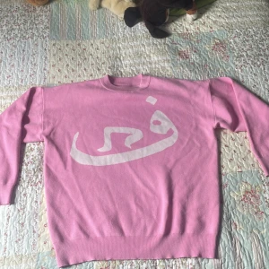 Rosa stickad tröja med vit print - Säljer en rosa stickad tröja med vit print framtill i ett coolt grafiskt mönster. Tröjan har rund hals och långa ärmar, perfekt för dig som gillar färg och vill sticka ut. Mjuk och skön känsla, passar till jeans eller kjol.