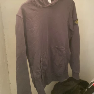Lila hoodie från Stone Island - Säljer en lila hoodie från Stone Island med klassisk patch på ärmen. Tröjan har huva, magficka och långa ärmar. Perfekt för dig som gillar streetwear och vill ha något stilrent men ändå unikt. Materialet är mjuk bomull som känns skönt mot huden. Pris kan diskuteras 