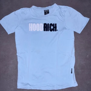 Ljusblå HOODRICH t-shirt XL barnstorlek - Snygg ljusblå t-shirt i XL barnstorlek från HOODRICH med broderad logga i vitt och svart på bröstet. Klassisk rund hals och korta ärmar. Skön passform och tillverkad i mjuk bomull, perfekt för en chill streetwear-look.