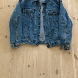 Klassisk blå jeansjacka - Säljer en klassisk blå jeansjacka med bronsfärgade knappar och två bröstfickor med lock. Inköpt på Beyond Retro. Jackan har en rak passform och är perfekt att slänga över en hoodie eller t-shirt. Tidlös modell som funkar till det mesta.