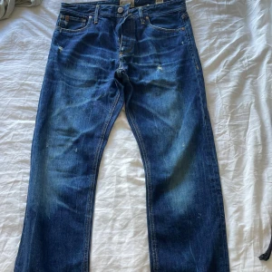 Blå jeans från Jack & Jones 32/32 - Säljer ett par klassiska blå jeans från Jack & Jones, modell Stan Original Premium Vintage. Jeansen har raka ben, fem fickor och snygga slitningar för en avslappnad look. Tillverkade i Italien i robust bomullstyg.