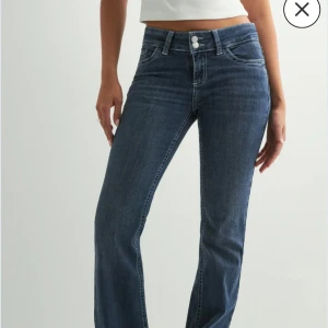 Blå bootcut jeans med broderade fickor - Snygga blå bootcut jeans med klassisk femficksdesign och coola broderade detaljer på bakfickorna. Jeansen har medelhög midja och stängs med dubbla knappar. Perfekta för dig som gillar en tidlös men trendig look.