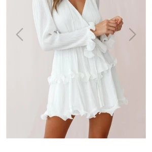 Studentklänning - Superfin vit kort omlottklänning från Dennis maglic med volangdetaljer och snöre i midjan (går att knyta hur man vill). Klänningen har långa ärmar, v-ringning och är gjord i ett lätt, plisserat tyg som ger en luftig känsla. Perfekt för sommarens alla tillfällen! Använd endast vid tre tillfällen, så den är i väldigt bra skick. Dock är där en liten defekt vid volangen men inget som syns. (Den var så när jag fick hem den!!) Nypris 899kr, mitt pris 750kr. Priset går att diskutera. 💕