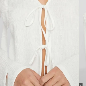 Vit knytblus från Vila - Superfin vit blus från Vila med lång ärm och v-ringning. Blusen har två knytband framtill och är gjord i ett lätt, strukturerat tyg som känns luftigt. Har bara användts en gång! Slutsåld online. Original pris 300. 