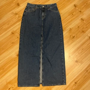 Mellanblå lång jeanskjol med slits - Säljer en mellanblå lång jeanskjol från bikbok med klassisk femficksdesign och snygg slits framtill. Hög midjad