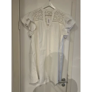 Vit kortklänning med volangärmar - Supersöt vit kortklänning från H&M med broderade detaljer upptill och volangärmar. Klänningen har v-ringad hals och är tillverkad i lätt bomullsmaterial som känns luftigt och fräscht. Perfekt för sommarens alla tillfällen när du vill känna dig extra fin.