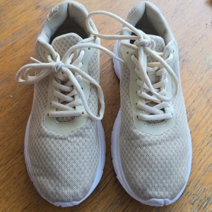 Beige sneakers med vit sula - Snygga beige sneakers med vit, rejäl sula och ovandel i mesh för extra andningsförmåga. Skorna har klassisk snörning och en sportig, stilren look som passar perfekt till jeans eller träningskläder. Lätta och bekväma för vardagsbruk eller träning.