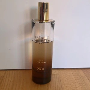Zara Caramel Temptation Parfym - Zara Caramel Temptation Eau de Parfum i en stilren, hög glasflaska med guldlock. Flaskan har en snygg brun ombre-effekt och text i guld. Doften är söt och karamellaktig, perfekt för dig som gillar gourmand-parfymer.