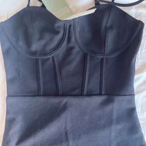 Svart långklänning med bustier - Snygg svart långklänning från H&M med bustier-inspirerad överdel och smala axelband. Klänningen har markerade sömmar framtill som ger en cool och strukturerad look. Materialet är mjukt och följsamt, perfekt för dig som gillar stilrena och trendiga plagg.