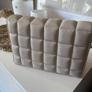 Beige quiltad axelväska i skinnimitation - Säljer en stilren beige axelväska🤎
