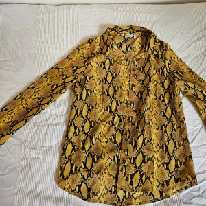 Gul ormskinnsmönstrad skjorta - Ormskinnsmönstrad gulsvart skjorta. Perfekt för animal print-älskaren, eller den coolaste office-siren på jobbet. (Färgen är mest lik första bilden, tydligt gul) 