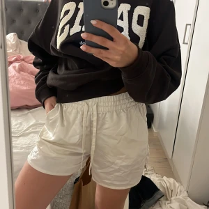 Vita satinskjorts med snörning - Snygga vita shorts i glansigt satinmaterial med elastisk midja och snörning. De har fickor på sidorna och en liten slits i benslutet för extra vibe. Perfekta för sommardagar när du vill vara både chill och stylish.