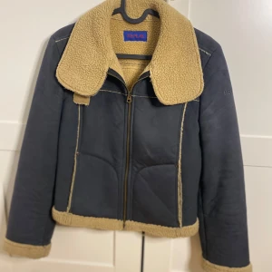 Replay teddy/mockajacka med dragkedja - Snygg teddy/mockajacka från Replay i mörkblått med beige fuskpälsfoder och krage. Jackan har en rak passform, långärmade ärmar och detaljerade sömmar. Dragkedja framtill och mjukt material som håller dig varm under kalla dagar. Jackan är vintage från slutet av 90-talet. 