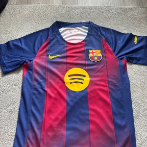 Fc Barcelona Hemma ställ 25/26 - Barcelona FC matchtröja från Nike i storlek S. Tröjan har klassiska blå och röda vertikala ränder, gult Nike-märke och Spotify-logga på bröstet. Tillverkad i lätt Dri-FIT polyester som andas, med klubbmärke broderat på vänster sida.