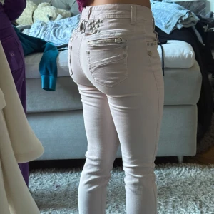 Ljusrosa raka jeans med detaljer - Säljer ett par ljusrosa raka jeans från Pangl med snygga silverfärgade dragkedjor och nitar vid fickorna. Low waist och figurnära passform, stretchigt material som sitter tajt. Perfekta för dig som gillar jeans med extra detaljer och en feminin touch.