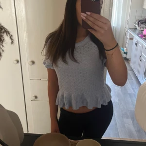 Ljusblå topp med volang H&M - Supersöt ljusblå stickad topp från H&M med korta ärmar och volangkant nertill. Perfekt för dig som gillar gulliga detaljer och en feminin vibe.