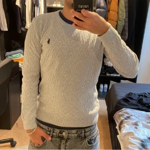 Ljusgrå stickad tröja från Ralph Lauren - En helt ny ralph lauren tröja som är använd bara två gånger med klassisk kabelstickning och rund hals. Tröjan har lång ärm och den ikoniska lilla broderade loggan på bröstet. Perfekt för dig som gillar stilren och enkel design.