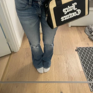 Juicy Couture beige och svart handväska - Säljer en snygg handväska från Juicy Couture i beige och svart med stort logotryck framtill. Väskan har svarta handtag, detaljer i syntet och dragkedja upptill. Insidan är fodrad i rosa tyg dock en fläck på insidan. Därav billigare pris.