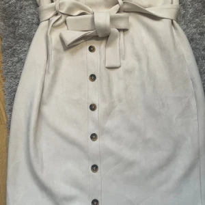 Beige kjol med bälte - Snygg beige kjol från Missguided med knappar framtill och ett bälte. Kjolen är lång och i mjukt material. Storlek 50,52. Aldrig använd. 60kr+frakt 