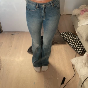 Blå bootcut jeans från Divided, stl 34 - Snygga blå bootcut jeans från Divided i storlek 34. Jeansen har klassisk femficksdesign, hög midja och lätt utsvängda ben. Materialet är äkta denim i bomull och de har slitna detaljer nertill. 