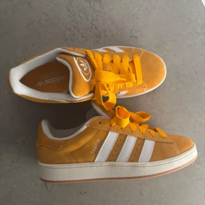 Adidas Campus sneakers i gul mocka - Adidas Campus sneakers i en riktigt snygg gul färg med klassiska vita ränder och vit sula. Ovandel i mjuk mocka, gula skosnören och extra vita snören medföljer. Skorna har en platt sula och rund tå, perfekt för dig som gillar retrostil.