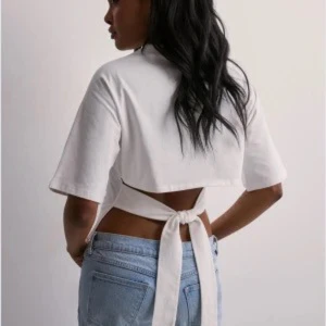 Vit knyt topp nelly - Säljer en vit croppad topp med korta ärmar och snygg knytning i ryggen. Toppen har en enkel, stilren design och är tillverkad i mjuk bomull. Perfekt för dig som gillar trendiga och bekväma plagg med en twist.