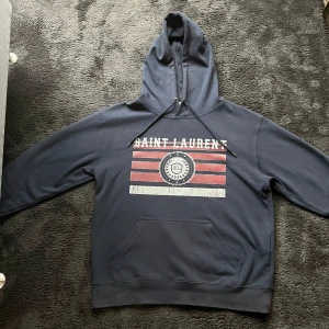 Mörkblå Saint Laurent hoodie - Säljer nu min snygga hoodie ifrån SL, tröjan är i ett bra skick och jag köpte den för ett halvårsen för 2300 och därav kan jag ej garantera äktenhet. Tröjan passar dig som är mellan 175-185! Hör av dig vid funderingar/bilder!!