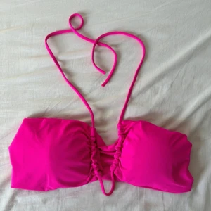 Rosa bikini med snörning. Funkar även topp - Säljer en chockrosa bikini med justerbara snören som kan knytas på flera olika sätt. Bikinin har bandeau-topp och medföljande guldfärgad ring för styling. Materialet är mjukt och stretchigt syntet, perfekt för stranden. Funkar även som en topp som passar perfekt till kjolar och shorts