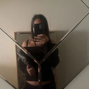 Svart ribbad offshoulder stickad tröja - Säljer en svart stickad tröja med ribbad struktur och offshoulder-modell. Tröjan har långa ärmar och sitter snyggt croppad över midjan. Perfekt för dig som gillar en trendig och stilren look.