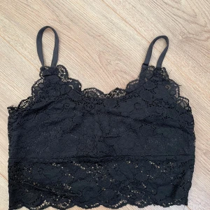 Svart spetslinnetopp från FB Sister - Supersnygg svart linnetopp från FB Sister med tunna axelband och vacker spets över hela toppen. Croppad modell med fina vågiga kanter och fodrad insida. Perfekt att styla med höga jeans eller kjol för en trendig look.
