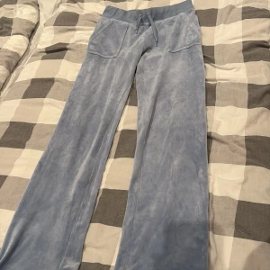 Blå velourbyxor Juicy Couture S - Supermjuka ljusblå mjukisbyxor från Juicy Couture i velour. Byxorna har bred resår i midjan med snörning, två stora fickor fram och broderad JC-logga på ena fickan. Perfekta för en chill och trendig look.
